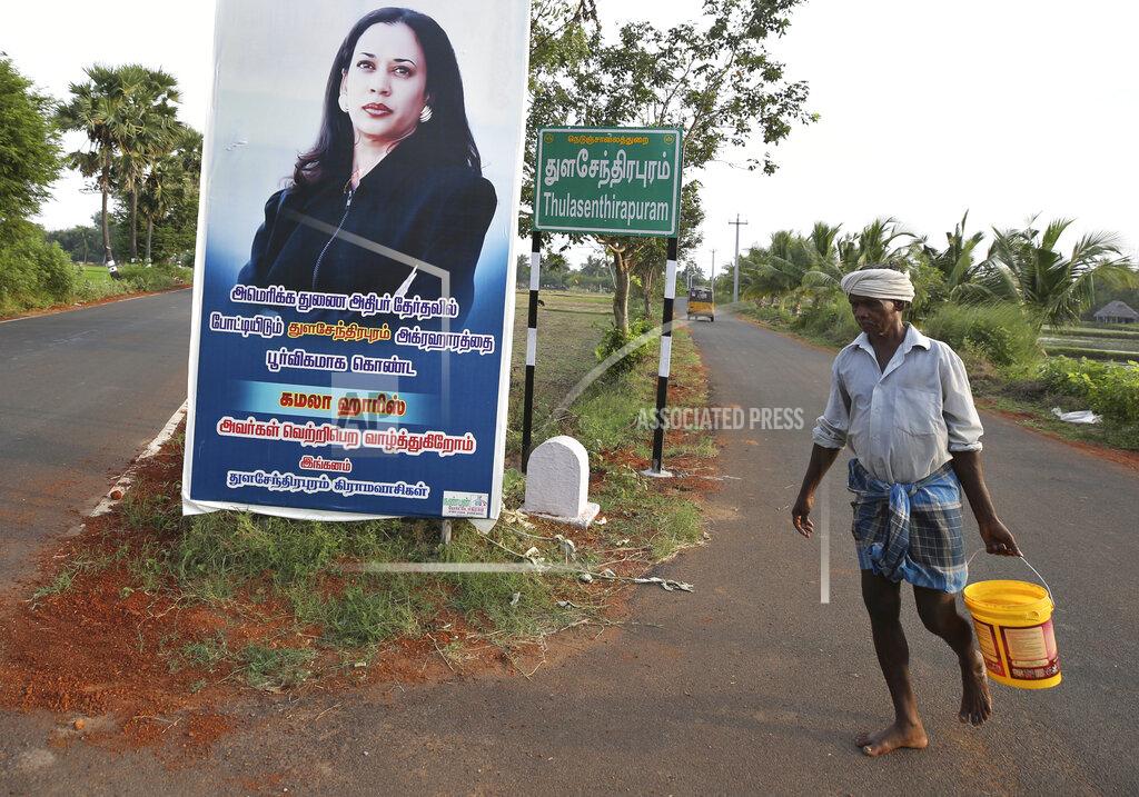 Aijaz Rahi A villager carries a bucket of water and walks past a hoarding featuring U.S. democratic vice presidential candidate Sen. Kamala Harris at a crossing in Thulasendrapuram village, south of Chennai, Tamil Nadu state, India, Wednesday, Nov. 4, 2020. The villagers on Tuesday held special prayers for Harris' success in the elections at the temple in this lush green village, the hometown of Harris' maternal grandfather who migrated from here decades ago. The hoarding in Tamil reads, "From Thulasendrapuram to America, we wish the American vice presidential candidate hailing from Thulasendrapuram village Kamala Harris victory in the elections- From the villagers of Thulasendrapuram." (AP Photo/Aijaz Rahi)