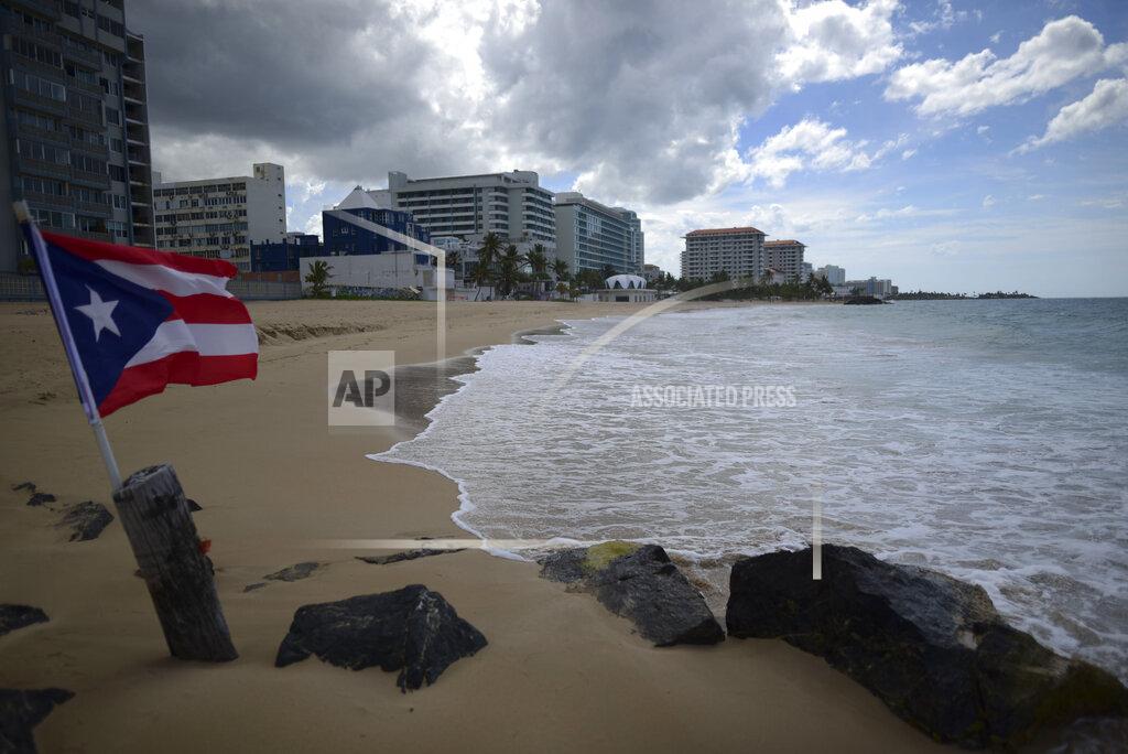 FILE - In this May 21, 2020 file photo, a Puerto Rican flag flies on an empty beach at Ocean Park, in San Juan, Puerto Rico. The number of tourists arrested in Puerto Rico on charges of violating COVID-19 measures is increasing as the U.S. territory cracks down on visitors who stay out past curfew and refuse to wear face masks or remain under quarantine, authorities said Tuesday, March 23, 2021. (AP Photo/Carlos Giusti, File)