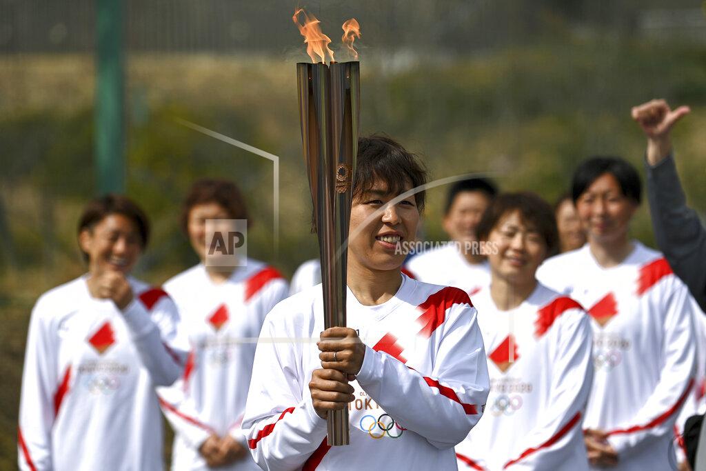 Philip Fong Japanese torchbearer Azusa Iwashimizu, center, a member of Japan women's national football team, arrives at a torch kiss point to pass on the flame during the torch relay grand start outside J-Village National Training Center in Naraha, Fukushima prefecture, northeastern Japan, Thursday, March 25, 2021. The torch relay for the postponed Tokyo Olympics began its 121-day journey across Japan on Thursday and is headed toward the opening ceremony in Tokyo on July 23. (Philip Fong/Pool Photo via AP)