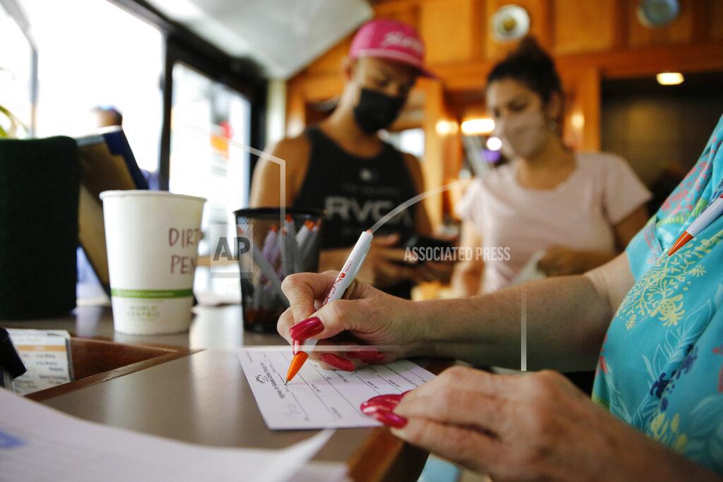 Caleb Jones Highway Inn restaurant hostess Ku'uipo Lorenzo, right, records contact information for Martin Day, left, and his wife, Ashley Day, center, after they showed proof of vaccination and a negative COVID-19 test result on Monday, Oct. 25, 2021, in Honolulu. To comply with local mandates, the restaurant requires all indoor diners to show proof of vaccination or have a recent negative test result before being seated. (AP Photo/Caleb Jones)