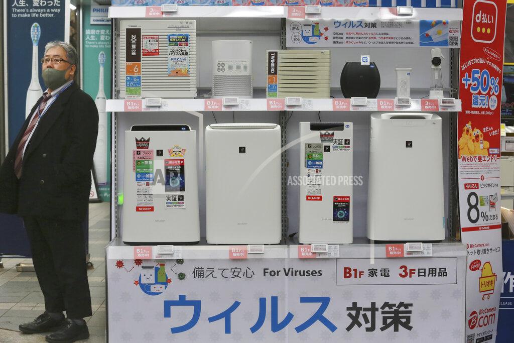 Koji Sasahara A man wearing a face mask to protest against the coronavirus stands beside a display of air cleaners at an electronics retailer in Tokyo, Tuesday, Jan. 12, 2021. The Tokyo area has been under a state of emergency since Friday to try to stop the spread of the virus. The banner at bottom reads: "Antivirus." (AP Photo/Koji Sasahara)