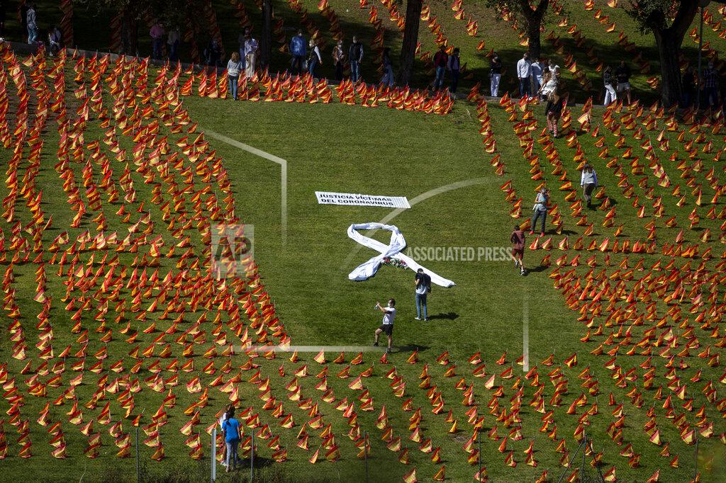 Manu Fernandez People walk among the Spanish flags placed in memory of coronavirus (COVID-19) victims in Madrid, Spain, Sunday, Sept. 27, 2020. An association of families of coronavirus victims has planted what it says are 53,000 small Spanish flags in a Madrid park to honor the dead of the pandemic. (AP Photo/Manu Fernandez)