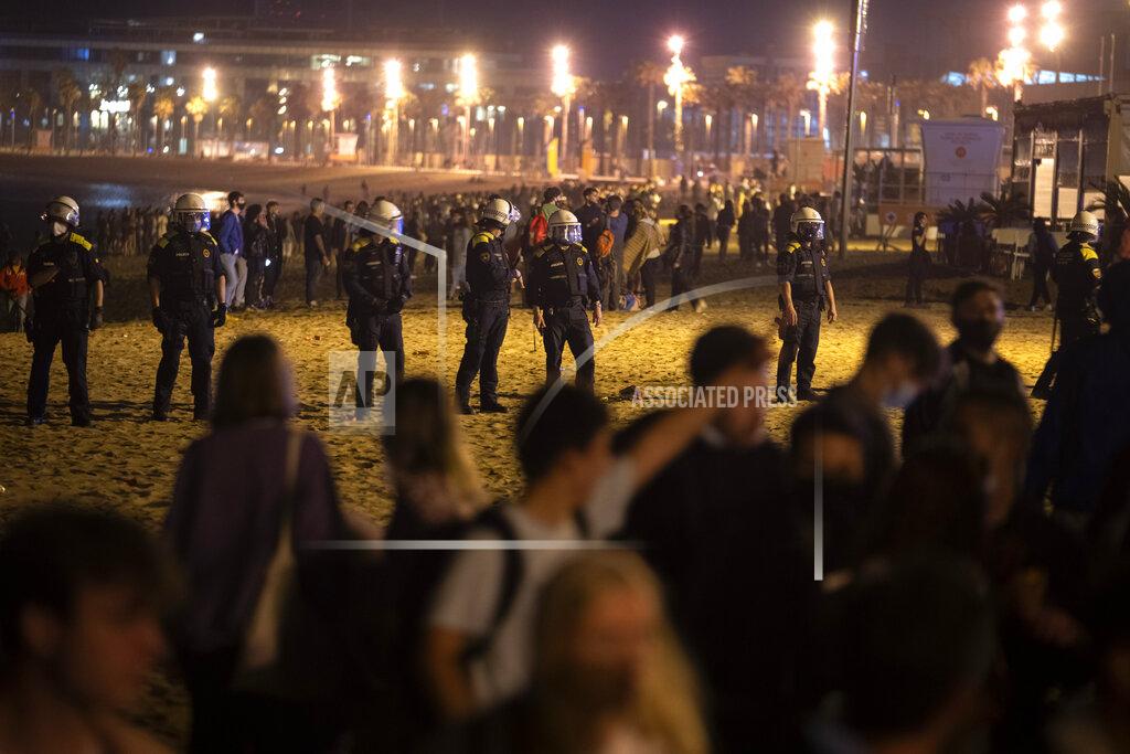 Emilio Morenatti Police officers stand guard as people crowded on the beach in Barcelona, Spain, Sunday, May 9, 2021. Barcelona residents were euphoric as the clock stroke midnight, ending a six-month-long national state of emergency and consequently, the local curfew. Spain is relaxing overall measures to contain the coronavirus this weekend, allowing residents to travel across regions, but some regional chiefs are complaining that a patchwork of approaches will replace the six-month-long national state of emergency that ends at midnight on Saturday. (AP Photo/Emilio Morenatti)
