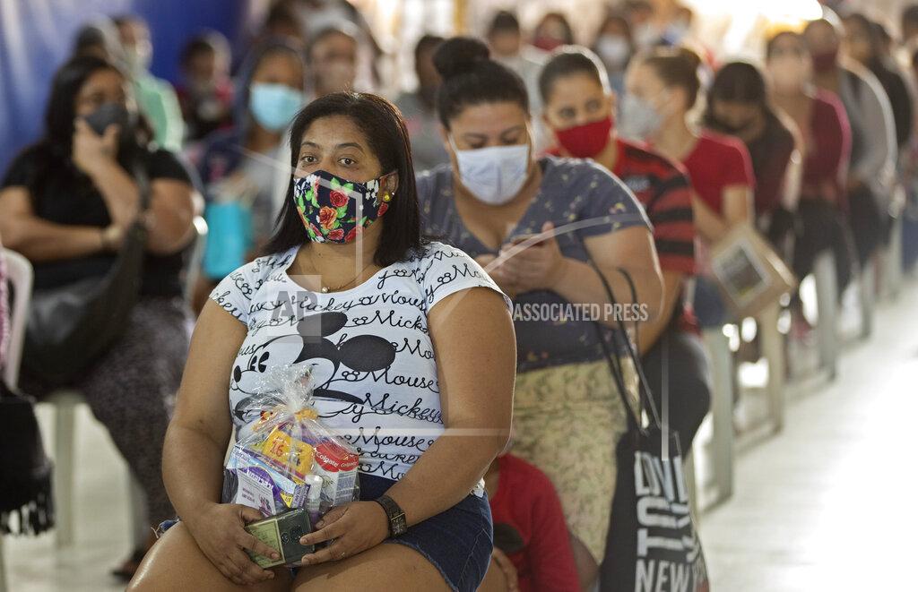 Andre Penner Women and girls sit after receiving a donation of sanitary napkins and other female hygiene supplies provided by the local NGO "G10 Favelas" amid the COVID-19 pandemic in the favela of Paraisopolis, in Sao Paulo, Brazil, Monday, May 24, 2021. (AP Photo/Andre Penner)