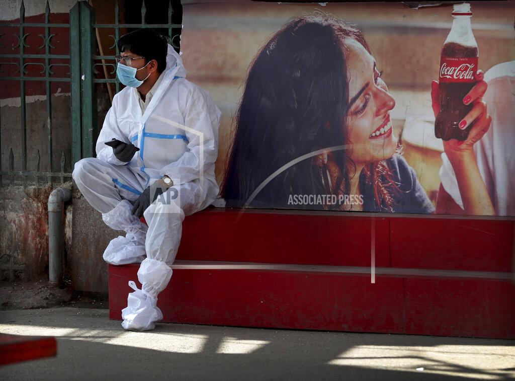 Aijaz Rahi A health worker wearing personal protective equipment takes a break as he awaits travelers to arrive outside a a train station in Bengaluru, India, Monday, Feb. 22, 2021. Cases of COVID-19 are increasing in some parts of India after months of a steady nationwide decline, prompting authorities to impose lockdowns and other virus restrictions. (AP Photo/Aijaz Rahi)