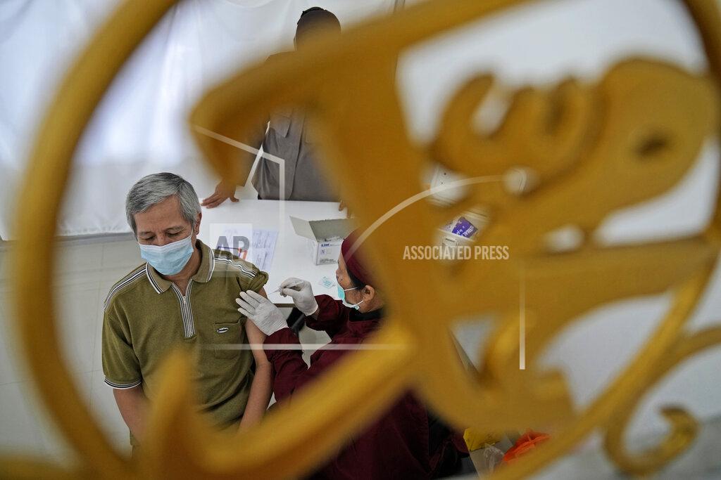 Dita Alangkara A man is seen through a mosque ornament in Arabic writing that reads: "Muhammad" as he receives a shot of the AstraZeneca vaccine for COVID-19 during a mass vaccination in Depok on the outskirts of Jakarta, Indonesia, Saturday, June 19, 2021. Indonesia, the world's fourth most populous country, aims to inoculate more than 181 million of its 270 million people by March 2022 but progress have been slow due to limited global vaccine supply, the unpreparedness of the national health system and vaccine hesitancy. (AP Photo/Dita Alangkara)