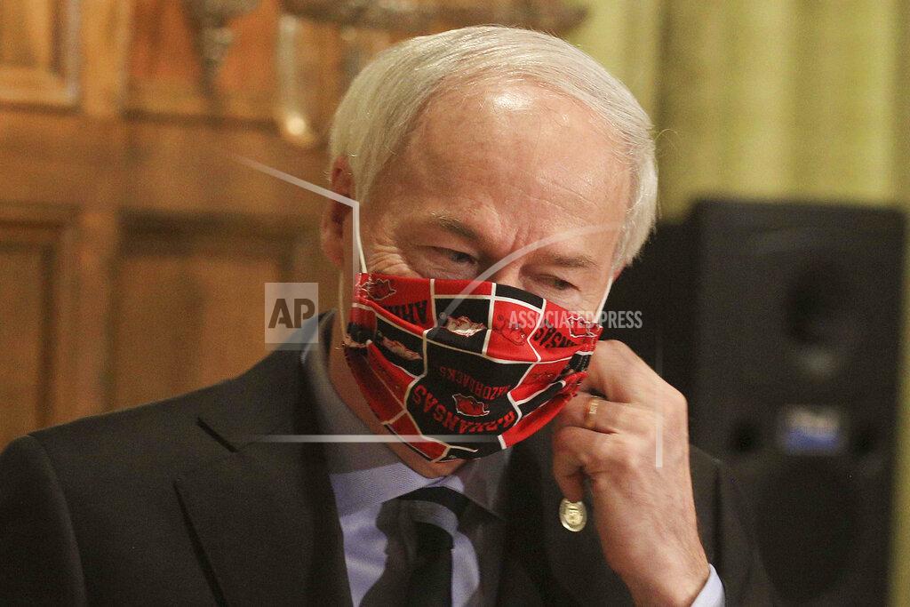 FILE - In this April 27, 2020 file photo, Gov. Asa Hutchinson takes off his Arkansas Razorbacks facemark as he arrives for the daily coronavirus briefing at the state Capitol in Little Rock. Hutchinson issued the order Thursday, July, 16, 2020, effective Monday, July 20, requiring people to wear masks in public throughout the state, which is dealing with a surge in coronavirus cases. The governor issued the order after weeks of resisting such a requirement. (Staton Breidenthal/Arkansas Democrat-Gazette via AP, File)