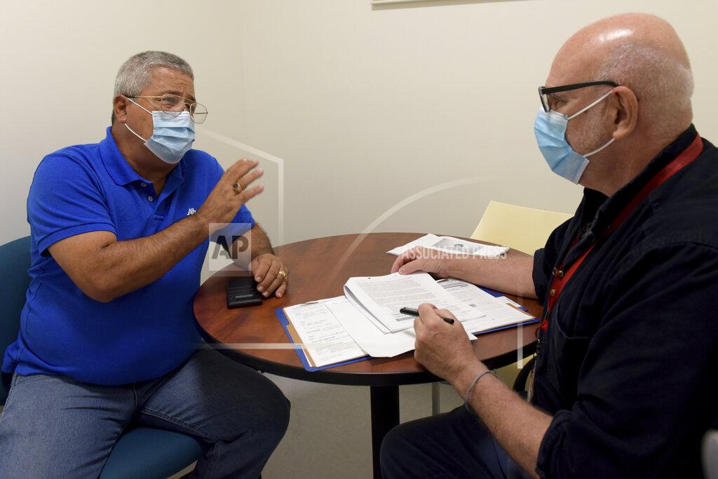 Juan Casuso, right, research coordinator from the University of Miami Miller School of Medicine, speaks with volunteer Julio Li during the intake process for Li to participate in testing for the National Institutes of Health-funded Moderna COVID-19 vaccine, Wednesday, Sept. 2, 2020 in Miami. Miami is one of 89 cities around the U.S., that's testing the Moderna COVID-19 vaccine. Study participants do not know if they're getting the vaccine or a placebo. (AP Photo/Taimy Alvarez)