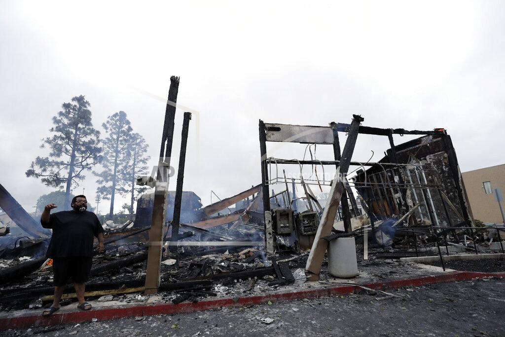 Gregory Bull A man stands in front of a bank that burned after a protest over the death of George Floyd, Sunday, May 31, 2020, in La Mesa, Calif. Protests were held in U.S. cities over the death of Floyd, a black man who died after being restrained by Minneapolis police officers on May 25. (AP Photo/Gregory Bull)