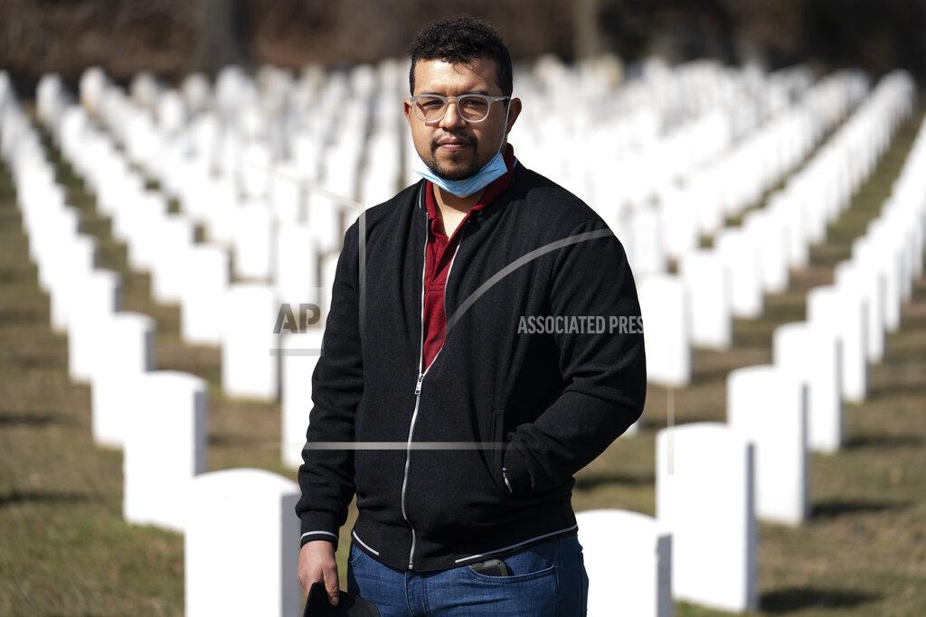 John Minchillo Undertaker Jesus Pujols stands for a portrait at Cypress Hills National Cemetery, Friday, March 12, 2021, in the Brooklyn borough of New York. Pujols hardly slept last spring. When he did, it was often in the van he used to transport the deceased. The 24-year-old works for a Brooklyn funeral home that at one point had nearly 500 people in its care, a backlog unresolved until June. (AP Photo/John Minchillo)