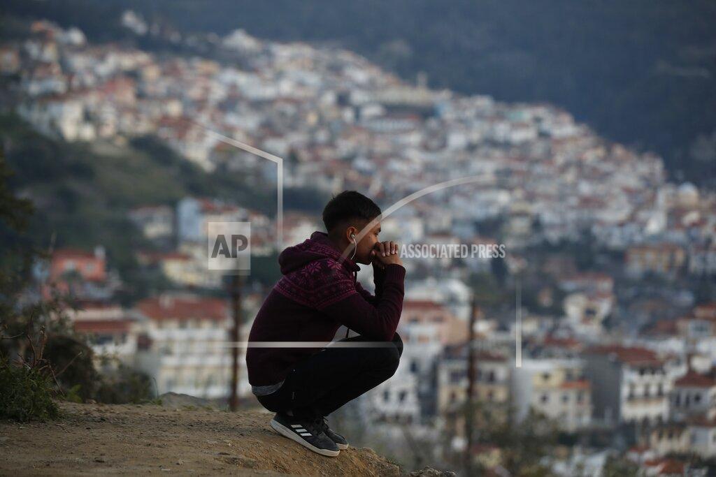 Thanassis Stavrakis A migrant sits on a hill outside the perimeter of the overcrowded refugee camp at the port of Vathy on the eastern Aegean island of Samos, Greece, Tuesday, Feb. 23, 2021. On a hill above a small island village, the sparkling blue of the Aegean just visible through the pine trees, lies a boy’s grave. His first ever boat ride was to be his last - the sea claimed him before his sixth birthday. His 25-year-old father, like so many before him, had hoped for a better life in Europe, far from the violence of his native Afghanistan. But his dreams were dashed on the rocks of Samos, a picturesque Greek island almost touching the Turkish coast. Still devastated from losing his only child, the father has now found himself charged with a felony count of child endangerment. (AP Photo/Thanassis Stavrakis)