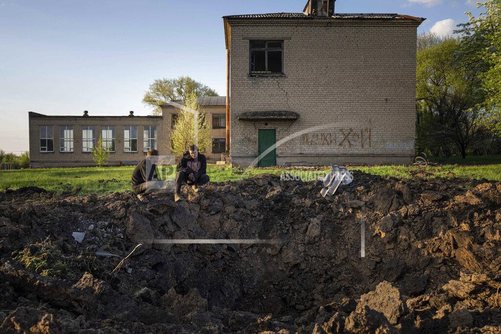 Evgeniy Maloletka FILE - People look at a crater created by a Russian rocket attack in a schoolyard in Dobropillya, Donetsk region, eastern Ukraine, Thursday, April 28, 2022. Despite the widespread damage and destruction to educational infrastructure, war crimes experts say proving an attacking military’s intent for individual schools is difficult. (AP Photo/Evgeniy Maloletka, File)