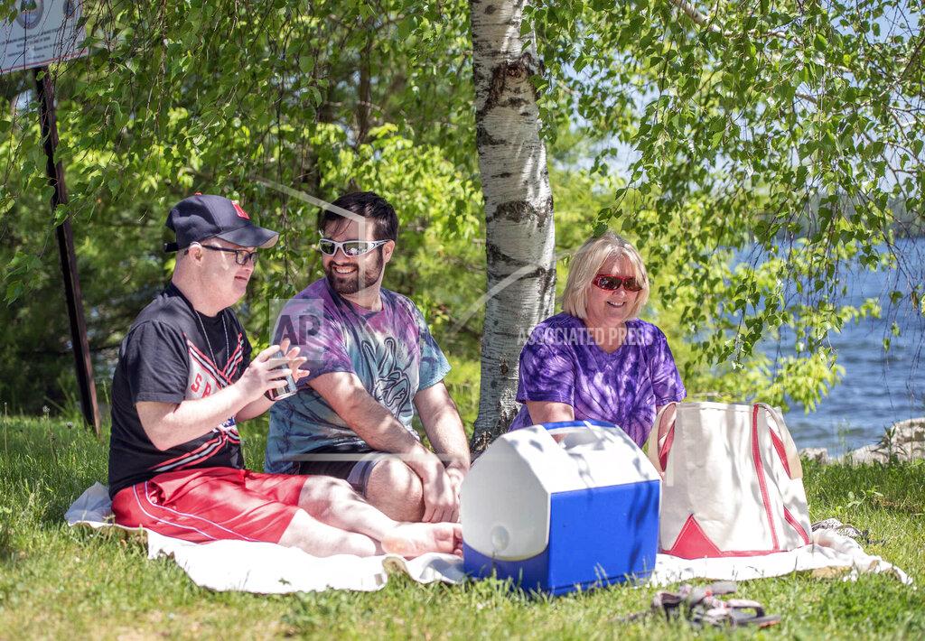 Ray, Drew and their mother Kim Masse, enjoy a picnic on the shores of Lake Auburn on Friday afternoon, May 29, 2020 in Lewiston, Maine. The three decided to get out of the house to enjoy the weather. As a household, they have been observing strict social distancing out of concern for family members health. They regularly do outdoor activities together, away from other people. (Andree Kehn/Sun Journal via AP)