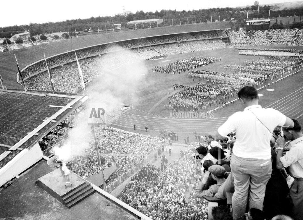Uncredited Australian athlete Ron Clark, bottom left, plunges the Olympic torch into the bronze bowl, to light the Olympic flame, which will burn throughout the XVI Olympic Games, in Melbourne, Australia, Nov. 22, 1956. (AP Photo)