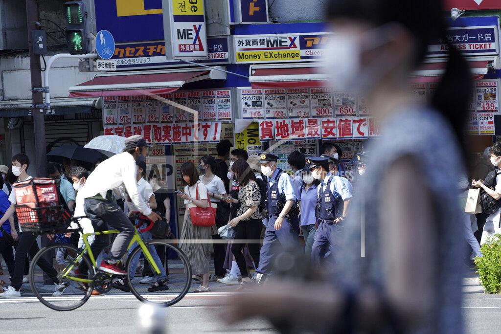Kantaro Komiya People and police officers wearing face masks to help curb the spread of the coronavirus walk past a busy crossing at Shinjuku district in Tokyo Friday, July 23, 2021, hours before the opening ceremony of the Summer Olympics starts. (AP Photo/Kantaro Komiya)