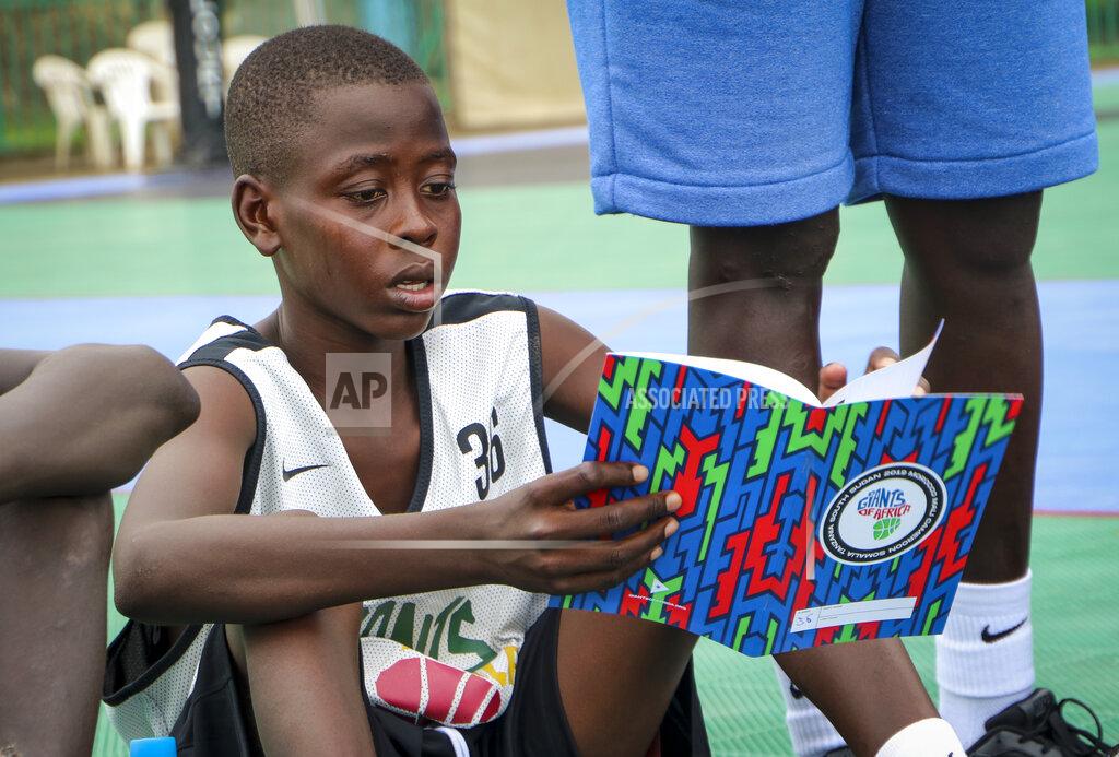 In this photo taken Tuesday, Aug. 20, 2019, a participant in the Giants of Africa basketball camp reads his career goals from a notebook while sitting on a basketball court in Juba, South Sudan. Masai Ujiri, president of the Toronto Raptors basketball team who won the NBA championship for the first time this year, is founder of the Giants of Africa non-profit organization which runs a three-day training camp in South Sudan to empower youth through basketball. (AP Photo/Sam Mednick)