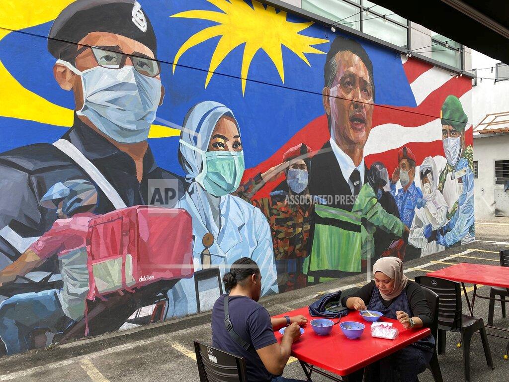 Vincent Thian A Malay couple have lunch next to a graffiti tribute to Malaysian workers on the frontlines against the COVID-19 coronavirus at Damansara in Selangor, outside Kuala Lumpur, Malaysia, Saturday, Nov. 7, 2020. Malaysia extended restricted movements in its biggest city Kuala Lumpur, neighboring Selangor state and the administrative capital of Putrajaya from Wednesday in an attempt to curb a sharp rise in coronavirus cases. (AP Photo/Vincent Thian)