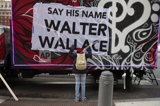FILE - In this Nov. 4, 2020, file photo, Sheila Rhames rests her hands on a banner honoring Walter Wallace Jr. in Philadelphia Wallace, a Black man, was shot and killed by police in West Philadelphia in October of 2020. Rhames was his neighbor. The Philadelphia Inquirer reported Tuesday, Oct. 26. 2021, the anniversary of the fatal police shooting of Wallace, that Philadelphia will spend $14 million to equip all of its officers with stun guns, train them on how to use them and require officers to wear them while on duty. (Joe Lamberti/Camden Courier-Post via AP, File)