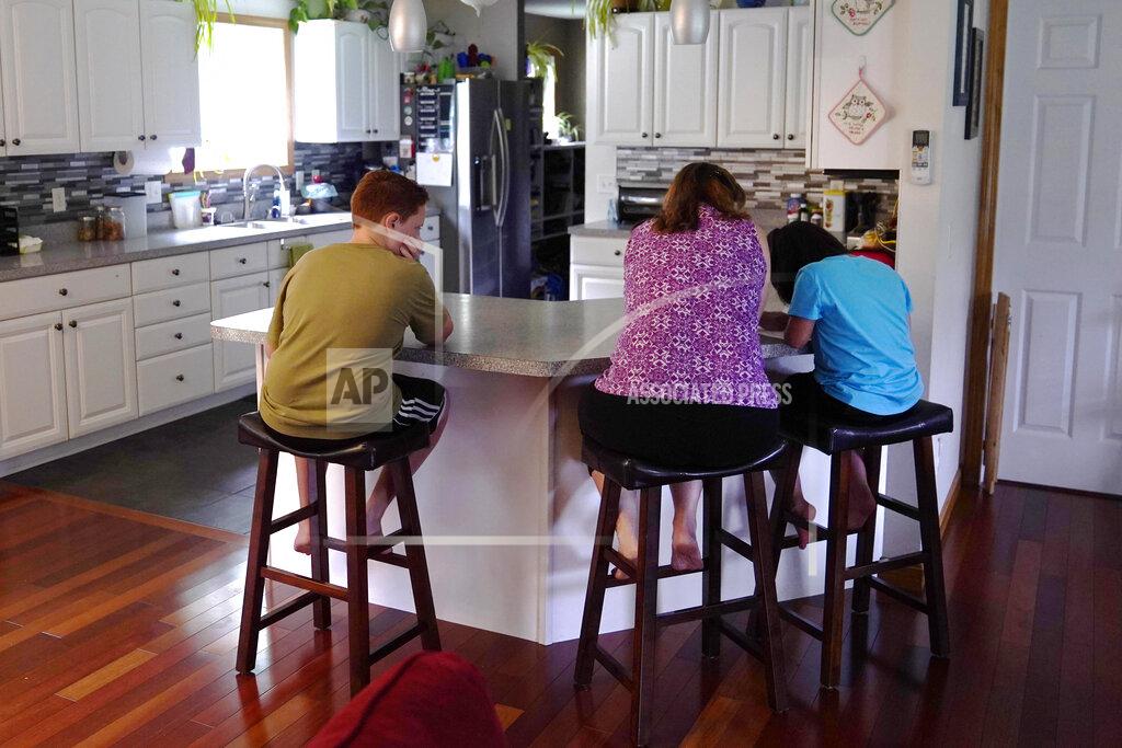 Charles Krupa Jennifer Osgood, center, helps her children Lily, 7, right, and Noah, 12, left, while studying at the kitchen counter in the family's home, Tuesday, July 20, 2021, in Fairfax, Vt. The Osgood children will continue to be homeschool this upcoming school year. As the pandemic took hold across the United States in the spring of 2020, it brought disruption and anxiety to most families. Yet some parents are grateful for one consequence: they are now opting to homeschool their children even as schools plan to resume in-person classes. (AP Photo/Charles Krupa)