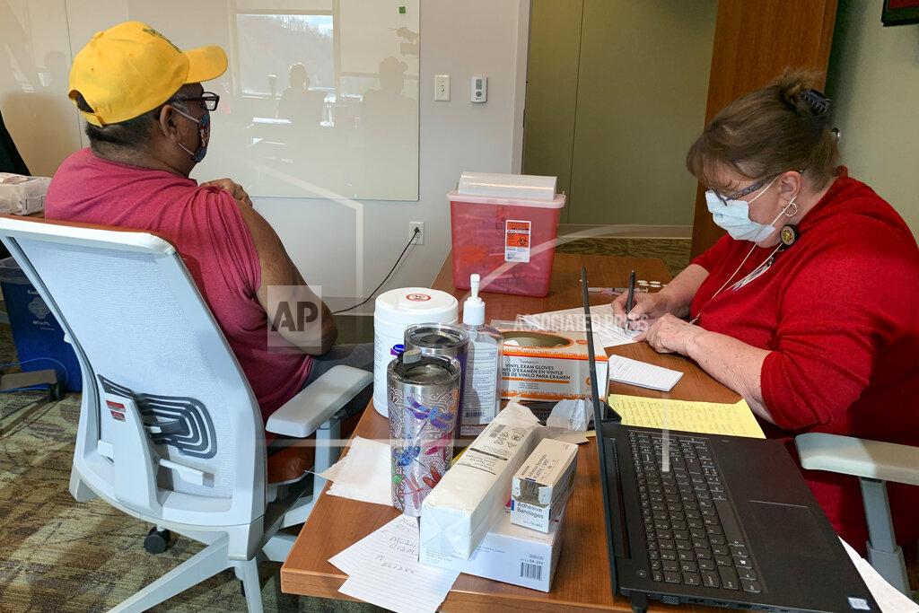 In this Thursday, Jan. 28, 2021 photo, a man rolls up his sleeve and prepares to receive the COVID-19 vaccine inside the hospital belonging to the Eastern Band of Cherokee Indians, in Cherokee , N.C. The native American tribe of 16,000 in Western North Carolina has faced little resistance while distributing the vaccine to tribal members. (AP Photo/Sarah Blake Morgan)