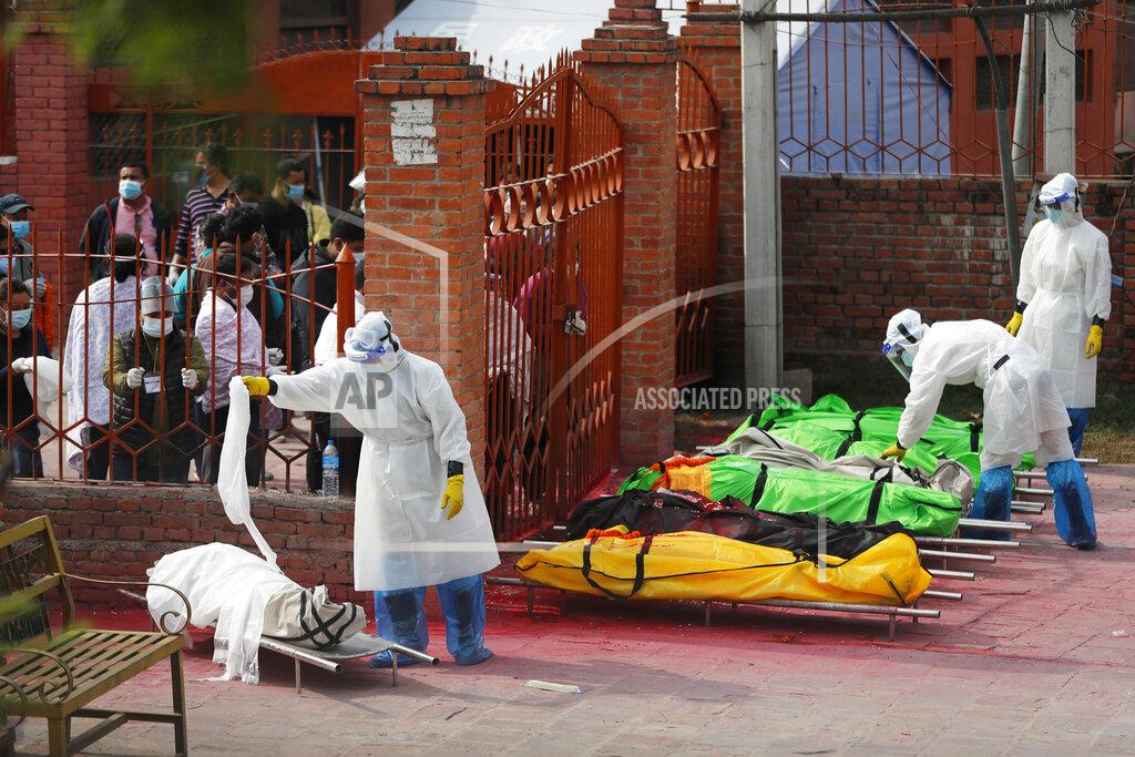 Niranjan Shrestha Family members watch as Nepalese army personnel in PPE suits prepare the bodies of COVID-19 victims for cremation near Pashupatinath temple in Kathmandu, Nepal, Friday, May 7, 2021. Across the border from a devastating surge in India, doctors in Nepal warned Friday of a major crisis as daily coronavirus cases hit a record and hospitals were running out of beds and oxygen. (AP Photo/Niranjan Shrestha)