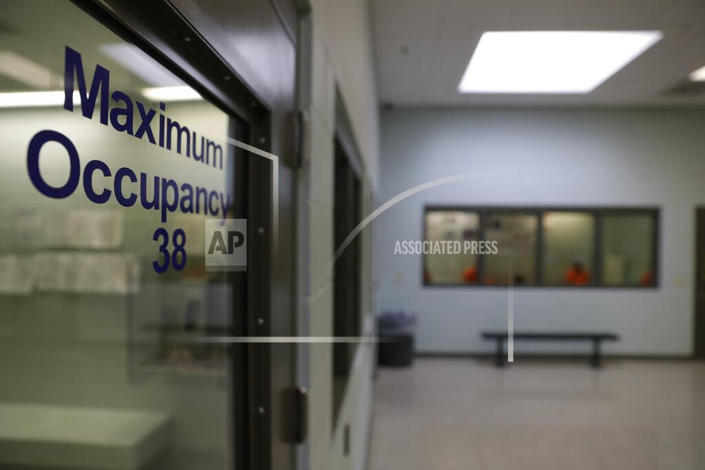 Chris Carlson FILE - In this Aug. 28, 2019, photo, detainees, background, wait to be processed at the Adelanto ICE Processing Center in Adelanto, Calif. In a wind-whipped California desert town, a sprawling facility can house nearly 2,000 immigrant detainees facing the prospect of deportation. These days, however, the privately-run detention center in Adelanto is nearly empty. (AP Photo/Chris Carlson, File)