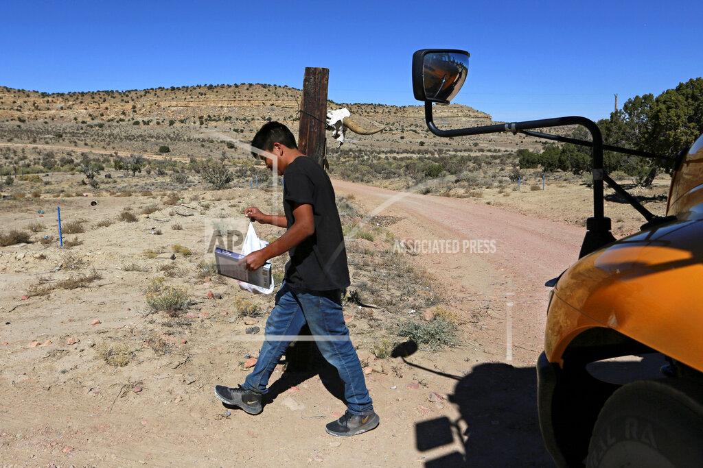 A student carries a math book delivered by school bus driver Kelly Maestas along his rural route outside Cuba, N.M., Oct. 19, 2020. The switch to remote learning in rural New Mexico has left some students profoundly isolated — cut off from others and the grid by sheer distance. The school system is sending school buses to students' far-flung homes to bring them assignments, meals and a little human contact. (AP Photo/Cedar Attanasio)