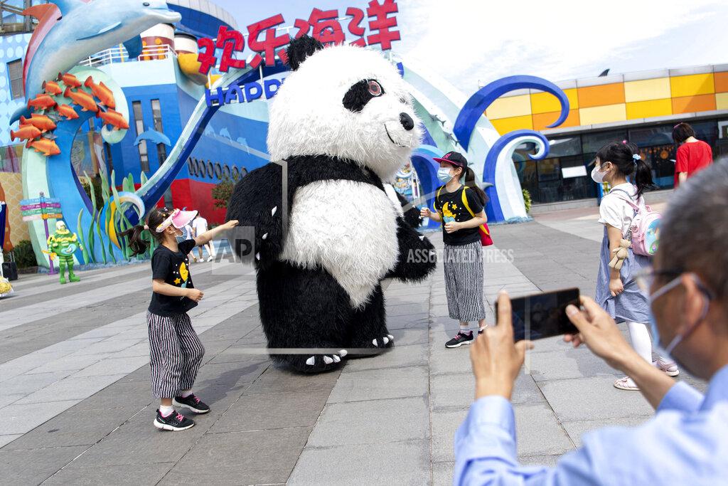 Xiong Qi In this, Tuesday, May 19, 2020, photo released by Xinhua News Agency, tourists wearing mask sas precaution against the coronavirus pose for photos with a panda mascot at the Happy Valley Wuhan theme park in Wuhan, in central China's Hubei Province, Happy Valley Wuhan, a theme park which had been closed due to the COVID-19 outbreak, has partly reopened on Tuesday with limitation on numbers and requiring online pre-booking. (Xiong Qi/Xinhua via AP)