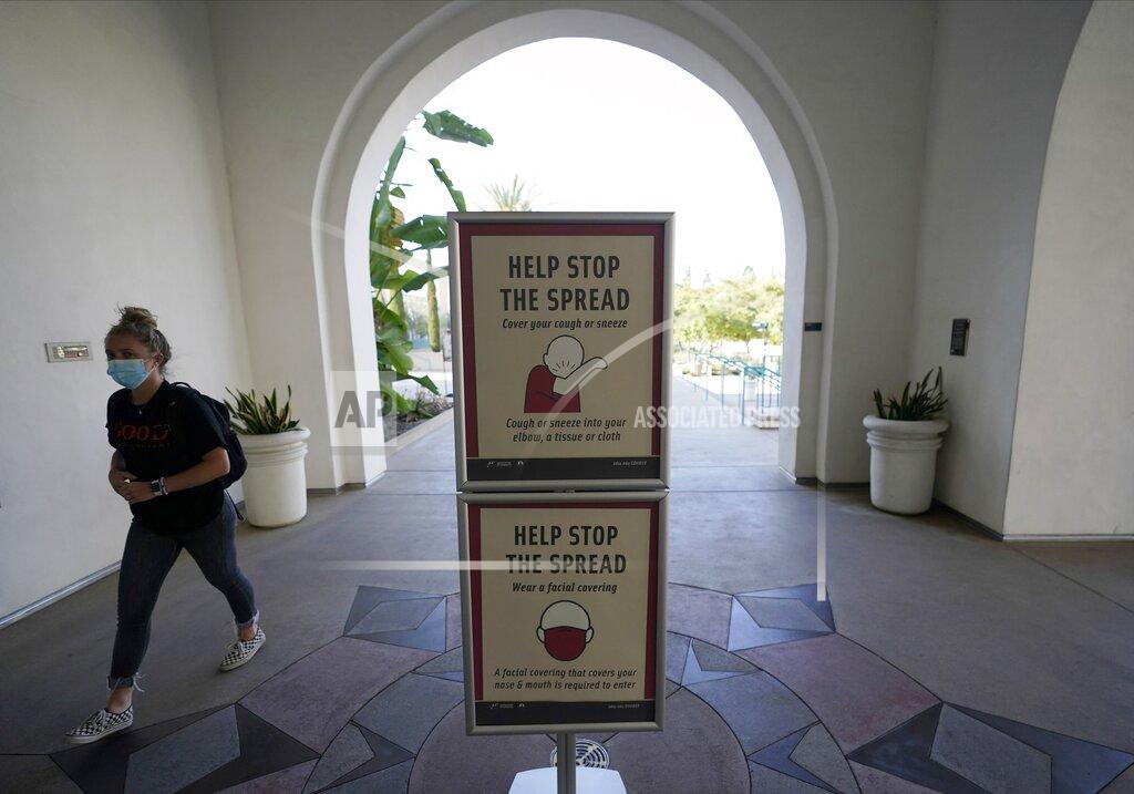 Gregory Bull FILE - In this Sept. 2, 2020, file photo, a woman wears a mask as she walks on campus at San Diego State University in San Diego. Colleges across the country are struggling to salvage the fall semester as campus coronavirus cases skyrocket and tensions with local health leaders flare. Schools have locked down dorms, imposed mask mandates, barred student fans from football games and toggled between online and in-person classes. (AP Photo/Gregory Bull, File)