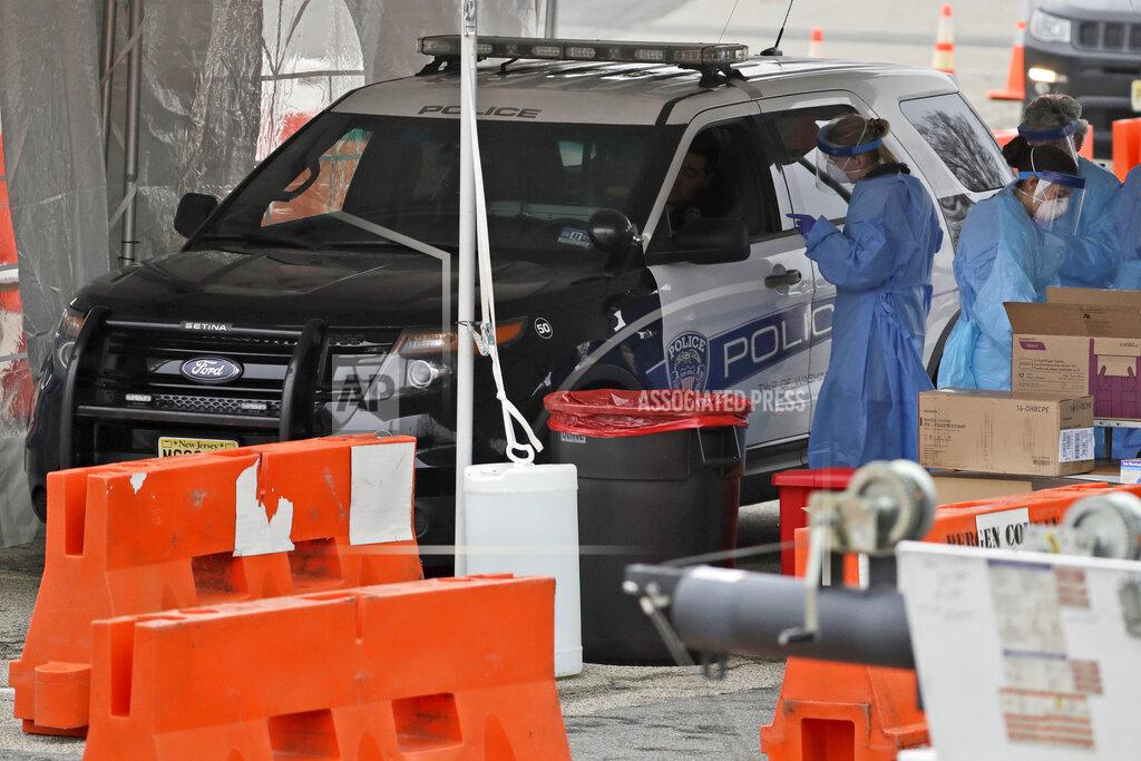 Seth Wenig FILE - In this March 20, 2020, file photo, a police officer drives through a COVID-19 testing center in Paramus, N.J. Detectives nationwide are grappling with changes the coronavirus has wrought on their investigations. Cold cases are getting colder, plainclothes investigators are digging out their dusty uniforms for patrol duty, and detectives are struggling to find new ways to connect with victims through thick masks. Even as police departments report major decreases in crime statistics thanks to stay-at-home orders, authorities say enough wrongdoing abounds to keep cops busy. And some detective work must still be in-person and hands-on, despite COVID-19. (AP Photo/Seth Wenig, File)