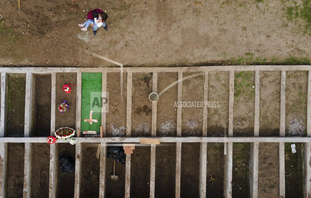 Esteban Felix Jose Collantes holds his daughter Kehity by the grave of his wife, her mother, Silvia Cano, who died of the new coronavirus at age 37, as they visit her grave one month after burying her at the Catholic Cemetery in Santiago, Chile, Wednesday, Aug. 5, 2020. “Daddy, daddy, why did mommy die?” asks his 5-year-old. "Because she was sick,” he answers, not knowing what to say but feeling he has to respond. (AP Photo/Esteban Felix)