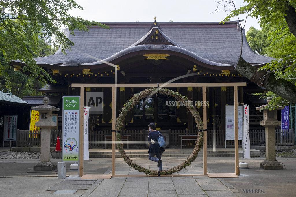 Kiichiro Sato A woman wearing a face mask steps through a Kaya wheel, a ring of woven grass, before praying at a Shinto shrine Friday, June 26, 2020, in Tokyo. The wheel marks the passage of the first half of the year and is used for prayers for the second half of the year. It also marks the beginning of summer at some Shinto shrines in Japan. (AP Photo/Kiichiro Sato)