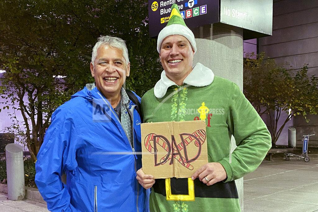 Rebecca Taylor Henning Doug Henning, right, who was adopted as a baby, poses with his biological father after meeting face to face for the first time on Tuesday, Nov. 24, 2020, at Logan International Airport in Boston. Henning, of Eliot, Maine, wore a costume like the one actor Will Ferrell's character wore in the movie "Elf" and he broke into the same awkward song from the movie while meeting his father. (Rebecca Taylor Henning via AP)
