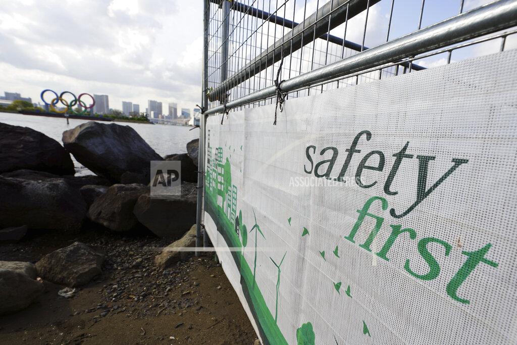 Eugene Hoshiko A construction fence featuring the words "Safety First" with a backdrop of the Olympic rings floating in the water in the Odaiba section Thursday, April 8, 2021, in Tokyo. The Tokyo Olympics are getting closer and things are starting to stir around the venues, though not as much as you might expect. Many preparations are still up in the air as organizers try to figure out how to hold the postponed games in the middle of a pandemic. (AP Photo/Eugene Hoshiko)