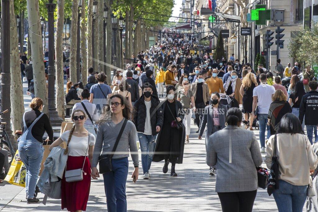 FILE - In this Saturday, May 16, 2020 file photo people wear face masks to help curb the spread of the coronavirus stroll along the Champs Elysees avenue in Paris. Britain will require all people arriving from France to isolate for 14 days - an announcement that throws the plans of tens of thousands of holiday makers into chaos. The government said late Thursday Aug. 13, 2020 that France is being removed from the list of nations exempted from quarantine requirements because of a rising number of coronavirus infections, which have surged by 66% in the past week. (AP Photo/Michel Euler, File)