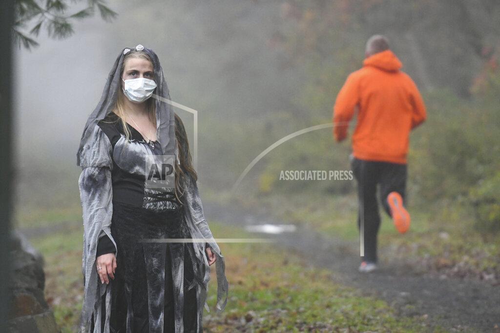 Jacqueline Dormer Rachel Adams, of Pottsville, Pa., portrays a zombie as a runner jogs past along the John B. Bartram trail during Schuylkill County's VISION's Spooky Schuylkill 5K Zombie Run/Walk in Landingville, Pa., on Saturday, Oct. 31, 2020. The event was held live and virtual. (Jacqueline Dormer/Republican-Herald via AP)