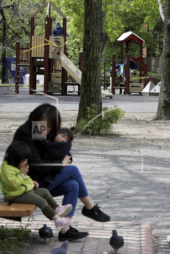 Gregorio Borgia In this April 24, 2020, photo, a woman sits with her children as workers in background apply ribbon reading, do not enter, sealing off a playground in Tokyo. Under Japan's coronavirus state of emergency, people have been asked to stay home. Many are not. Some still have to commute to their jobs despite risks of infection, while others are dining out, picnicking in parks and crowding into grocery stores with scant regard for social distancing. (AP Photo/Gregorio Borgia)