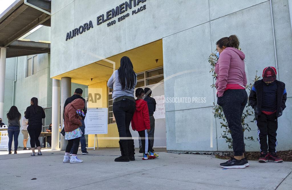 Damian Dovarganes In this Tuesday, March 16, 2021, photo, parents and students line up to pick up school materials outside the Aurora Elementary School in Los Angeles. Students in California classrooms can sit 3 feet apart instead of 6 under new guidelines adopted by the state as school officials figure out how to reopen campuses closed for a year during the coronavirus pandemic. (AP Photo/Damian Dovarganes)