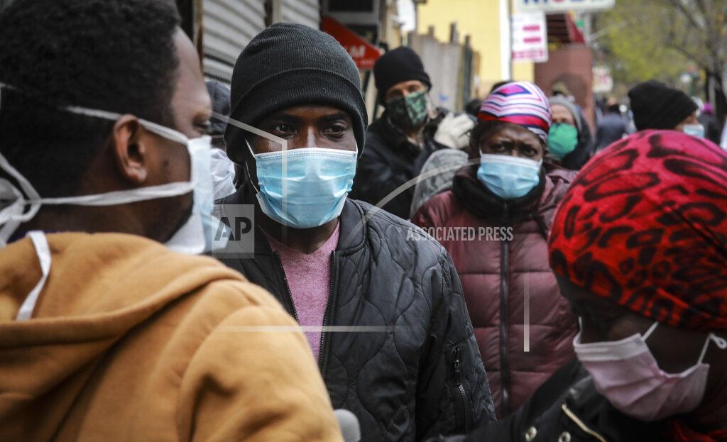 People wait for a distribution of masks and food from the Rev. Al Sharpton in the Harlem neighborhood of New York, after a new state mandate was issued requiring residents to wear face coverings in public due to COVID-19, Saturday, April 18, 2020. "Inner-city residents must follow this mandate to ensure public health and safety," said Sharpton. The latest Associated Press analysis of available data shows that nearly one-third of those who have died from the coronavirus are African American, even though blacks are only about 14% of the population. (AP Photo/Bebeto Matthews)