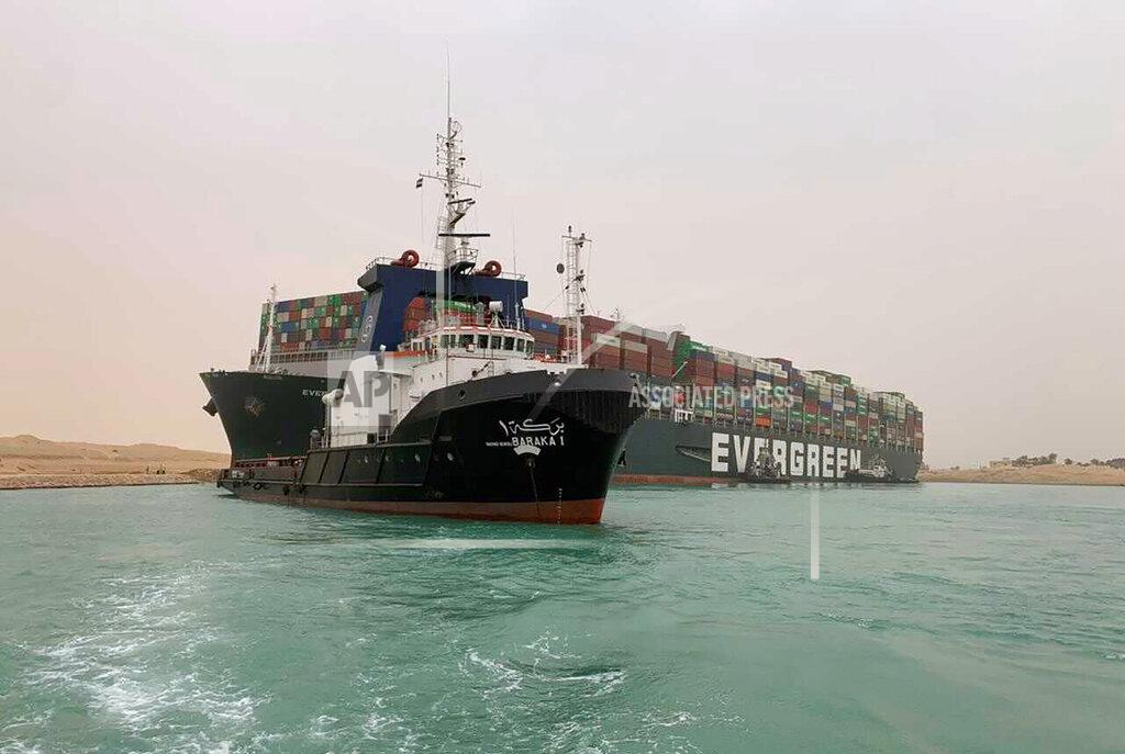 Uncredited CORRECTS NAME OF SHIP TO EVER GIVEN, NOT EVER GREEN - In this photo released by the Suez Canal Authority, a boat navigates in front of a cargo ship, Ever Given, Wednesday, March 24, 2021, after it become wedged across Egypt’s Suez Canal and blocked all traffic in the vital waterway. An Egyptian official warned Wednesday it could take at least two days to clear the ship. (Suez Canal Authority via AP)