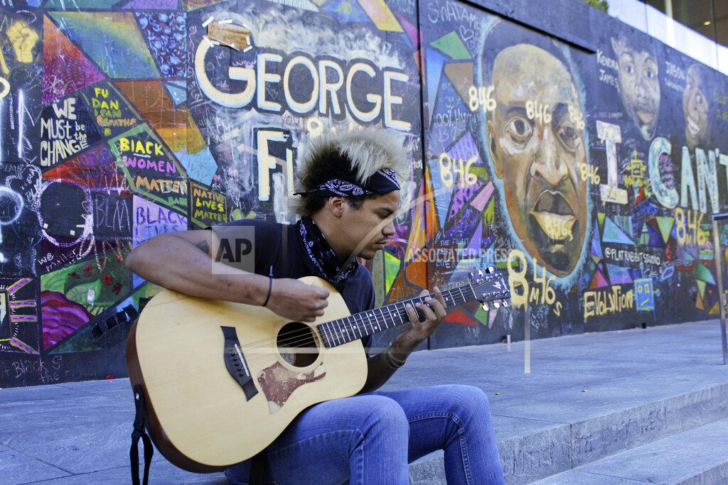 Gillian Flaccus Shane Braswell, who has participated in Black Lives Matter protests this summer, plays guitar in front of a mural covering the entrance to an Apple store, Aug. 27, 2020 in Portland, Ore. Braswell said President Donald Trump's portrayal of Portland as a violent city overcome by mobs of protesters is inaccurate and grossly exaggerated. "I hate when people say, 'Portland riots' or 'Seattle riots.' You see it as a riot because it is something that's going against your administration or your beliefs or your principles when the majority of the country is fed up and marching arm-in-arm," he said. (AP Photo/Gillian Flaccus)