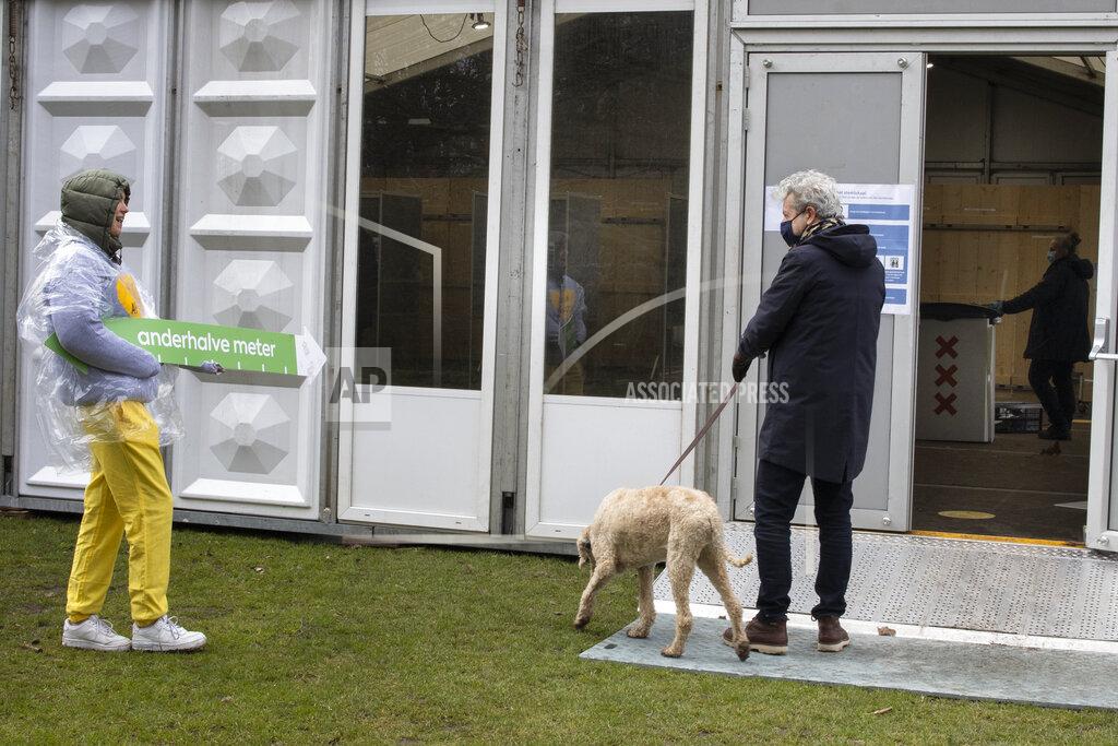 Peter Dejong A volunteer at a polling station wearing a sweatshirt emblazoned with a yellow heart and the text "keep your distance" holds an arrow measuring out the 1.5-meter social distance as a voter enters to cast his ballot in Amsterdam, Netherlands, Monday, March 15, 2021. Polling stations opened across the Netherlands early Monday in a general election that has been spread over three days to allow people to vote safely during the coronavirus pandemic. (AP Photo/Peter Dejong)