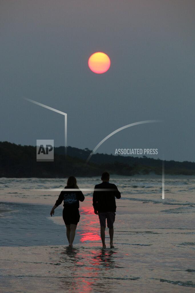 Mark Rogers A couple walks along the beach in Cherry Grove, S.C., early Thursday, July 22, 2021. Smoke from wildfires in the western U.S. and Canada is blanketing much of the continent, including thousands of miles away on the East Coast. And experts say the phenomenon is becoming more common as human-caused global warming stokes bigger and more intense blazes. (Mark Rogers/The Sanford Herald via AP)