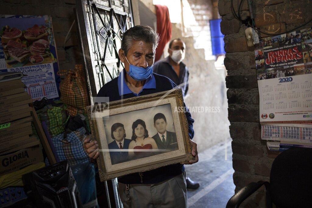 Teodoro Mejia holds a portrait of himself, at right, with his wife Berta Cusi Palomino, moments after funeral home workers removed her body from their home, where according to Mejia she died of COVID-19, in Lima, Peru, Thursday, May 14, 2020. At left in the photo is Berta's brother
Edgar. Peruvian authorities and the Pan American Health Organization are investigating whether the country failed to classify just over 27,000 deaths as caused by the novel coronavirus, a figure that could more than double the country's official death toll from the disease. (AP Photo/Rodrigo Abd)
