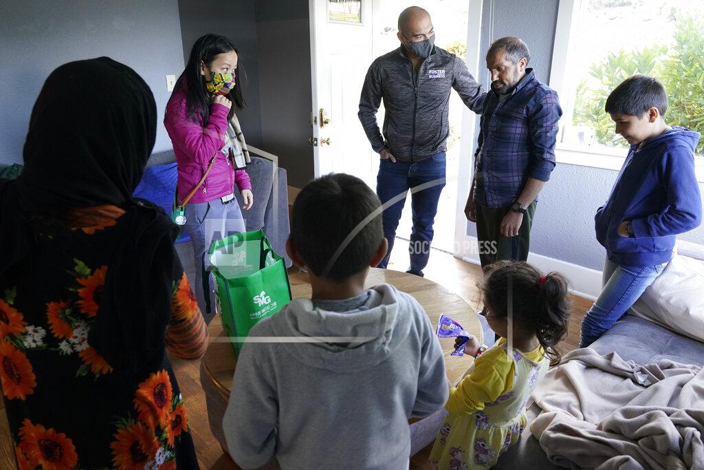 Ted S. Warren Thuy Do, second from left, and her husband, Jesse Robbins, center, talk with Abdul, second from right, and his family, after they stopped by the vacant rental home they own in Seattle, Monday, Sept. 20, 2021, to drop off produce from their garden and check on the family. Abdul worked as a mechanic before leaving Kabul, Afghanistan about a month ago, and Do and Robbins have provided the house as a place for them live until they can find more permanent housing. Do was nine years old when her family arrived in the United States from Vietnam in the 1980s, and that memory led Do and Robbins to reach out to assist Afghans fleeing their country. (AP Photo/Ted S. Warren)