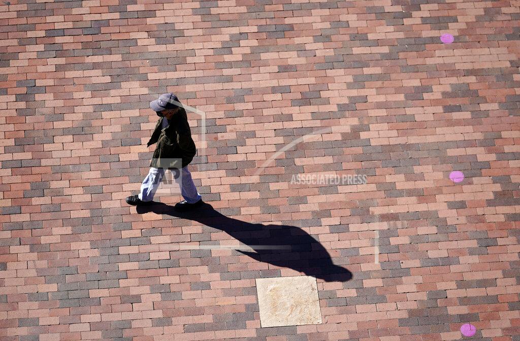 David Zalubowski FILE - In this April 8, 2021, file photo a lone pedestrian casts a long shadow while passing through the plaza in front of the gate top Coors Field at the corner of 20th Street and Blake early in Denver. Millions of Americans are struggling through life with few people they can trust for personal and professional help, a disconnect that raises a key barrier to recovery from the social, emotional and economic fallout of the pandemic. That's according to a new poll from Impact Genome and The Associated Press-NORC Center for Public Affairs Research. (AP Photo/David Zalubowski, File)