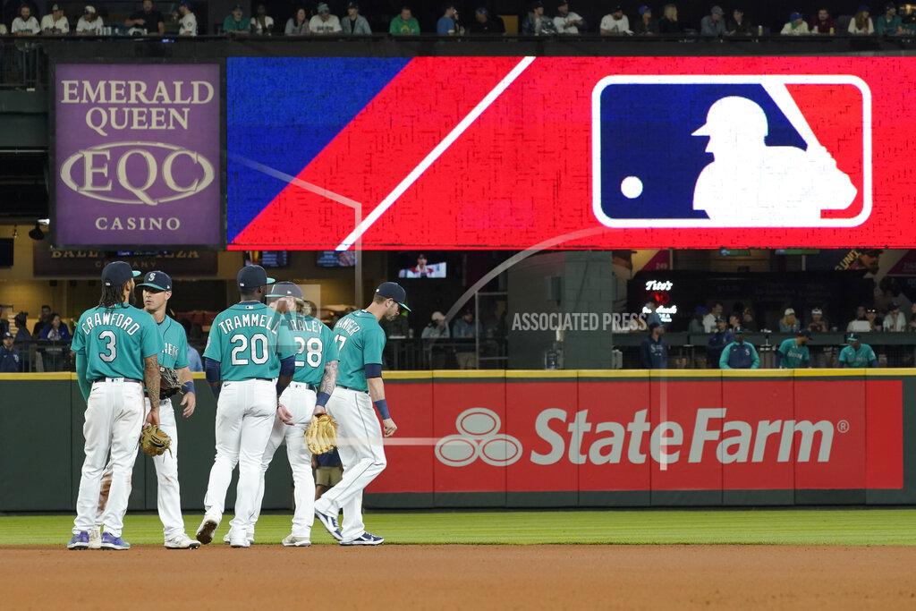 Ted S. Warren FILE - Seattle Mariners gather as the MLB logo is shown during a review of an attempted catch by right fielder Mitch Haniger of a ball hit by Tampa Bay Rays' Ji-Man Choi that was originally called an out during the ninth inning of a baseball game Friday, June 18, 2021, in Seattle. The call was overturned. While Major League Baseball and the players union try to chart a path forward, hoping to get baseball back on the field, some experts are watching the talks more from an academic viewpoint. (AP Photo/Ted S. Warren)