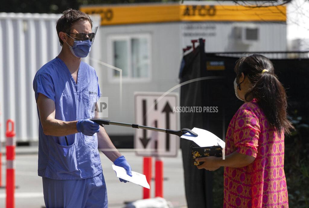 Darryl Dyck A healthcare worker uses a grabber to hand a woman a piece of paper at a COVID-19 testing facility during the coronavirus pandemic in Burnaby, British Columbia, on Thursday, Aug. 13, 2020. (Darryl Dyck/The Canadian Press via AP)