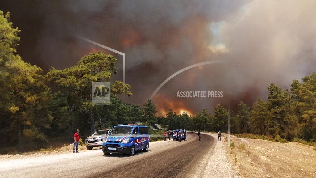 Arif Kaplan Paramilitary police officers and people watch as a wildfire fanned by strong winds rage near the Mediterranean coastal town of Manavgat, Antalya, Turkey, Wednesday, July 28, 2021. Authorities evacuated homes in Manavgat as a wildfire raged Wednesday through a forest. Gendarmerie forces helped move residents out of four neighborhoods in the town out of the fire's path as firefighters worked to control the blaze, the Manavgat district governor Mustafa Yigit told the state-run Anadolu Agency. (Arif Kaplan/IHA via AP)