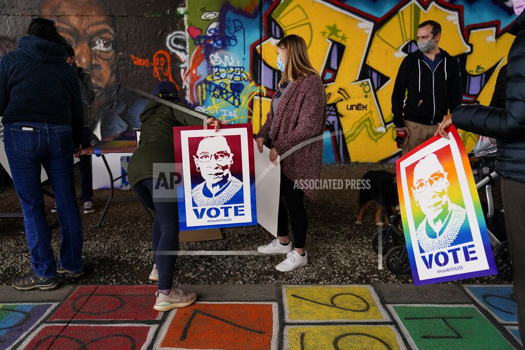 Brynn Anderson People wait in line holding Supreme Court Justice Ruth Bader Ginsburg posters and wait for artist Brandon Litman to paint a campaign poster after Georgia's Senate runoff race on Sunday, Jan. 10, 2021, in Atlanta. (AP Photo/Brynn Anderson)